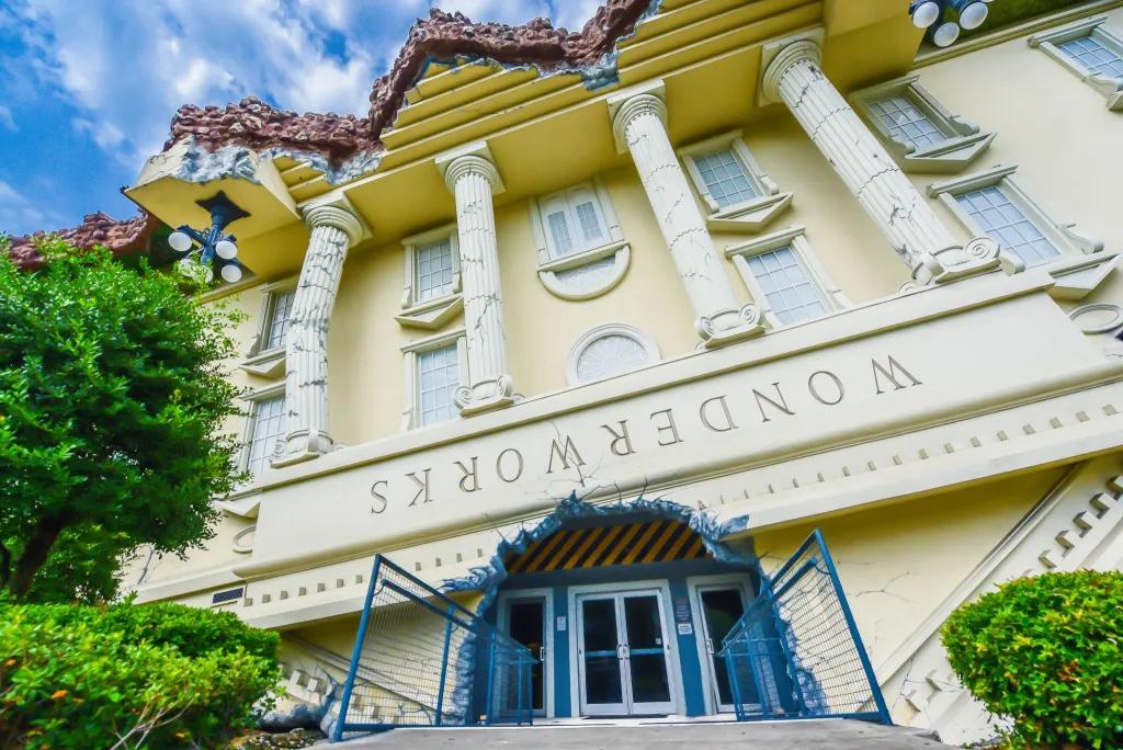 A white mansion overturned upside down with cracked white pillars. There is a hole in the house which is cut out for the main entrance.