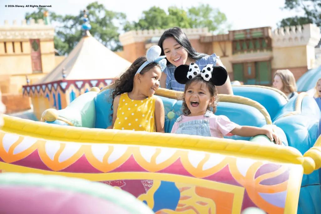 Two young girls sat in front of a woman smiling while riding the Flying Carpets ride at Disney World