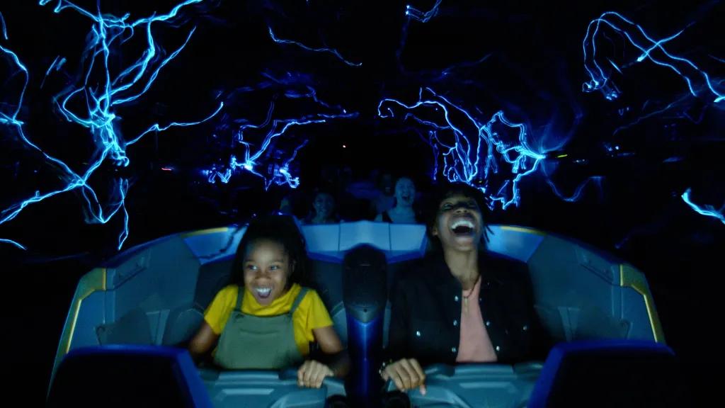 Two guests smiling and gasping holding onto lap restraints as they are launched backwards. There are blue electrical lines surrounding them.