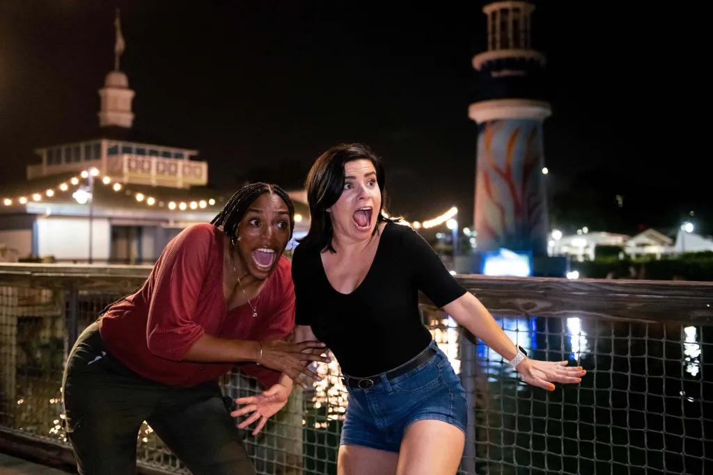 Two women clutching onto one another and screaming at something off camera with a large lake and the iconic SeaWorld lighthouse in the background.