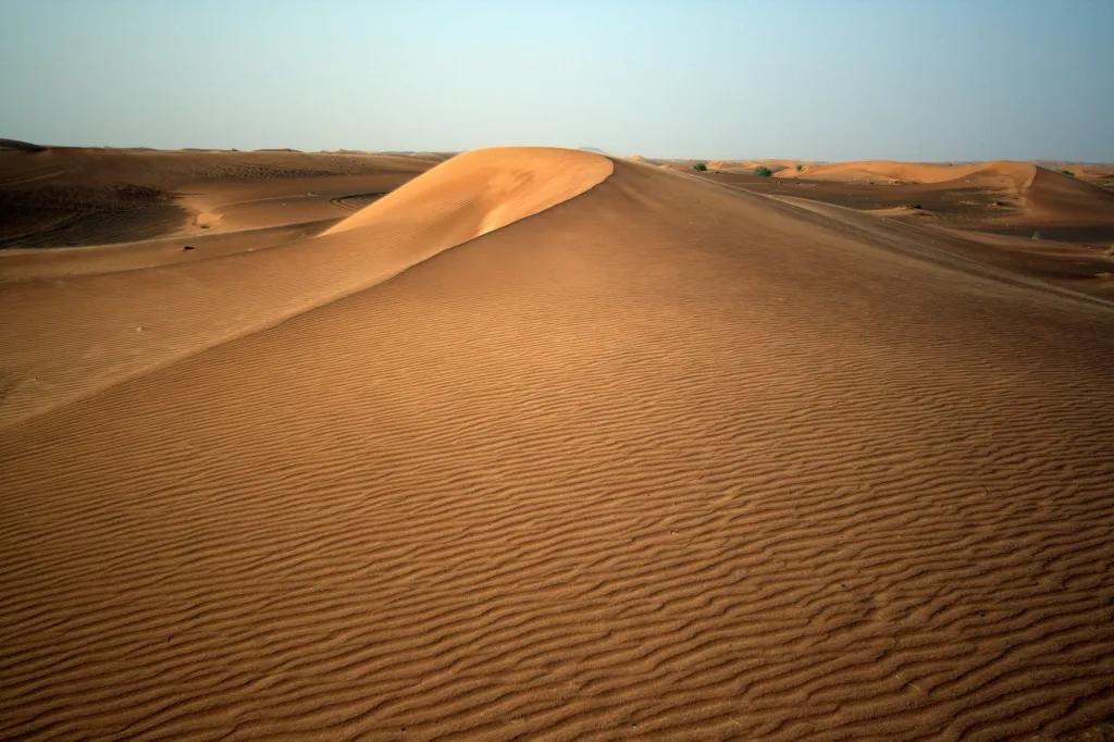 A large sand dune in the middle of the desert with a clear blue sky above.