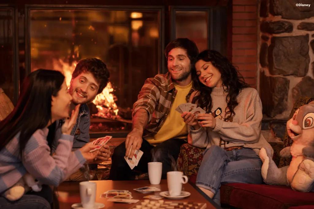 A group of friends say next to a fireplace playing cards around a table