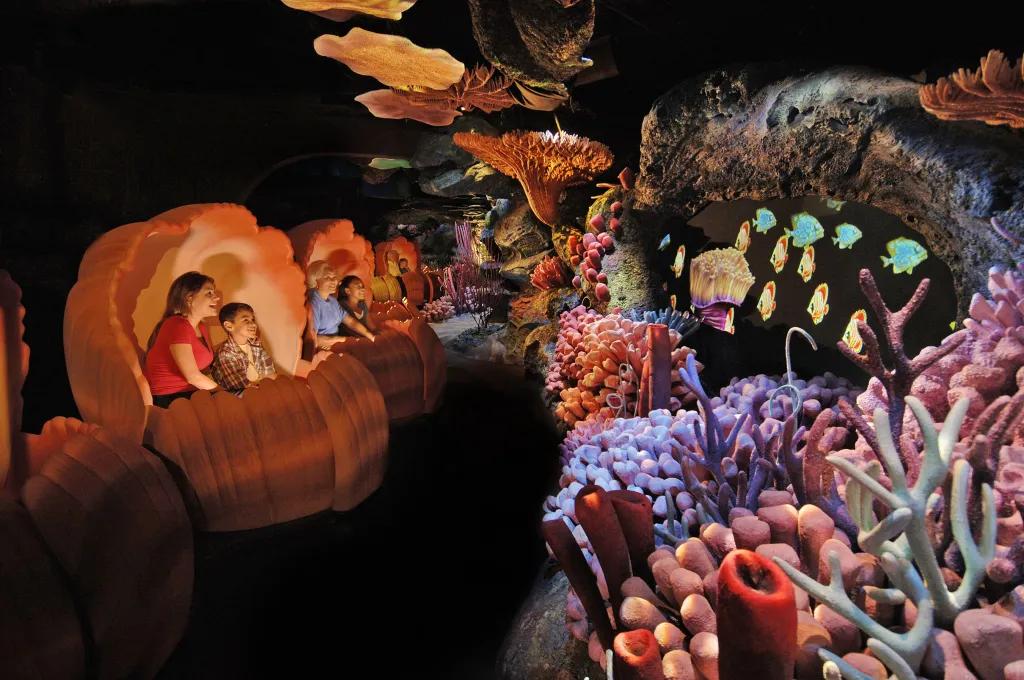 Guests sat in clam shell ride vehicles looking over to coral reefs and projections of fish swimming.