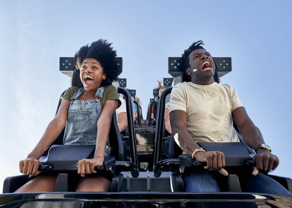 Two people screaming on a rollercoaster with only lap bars holding them in. They are looking down in shock ready to fall.