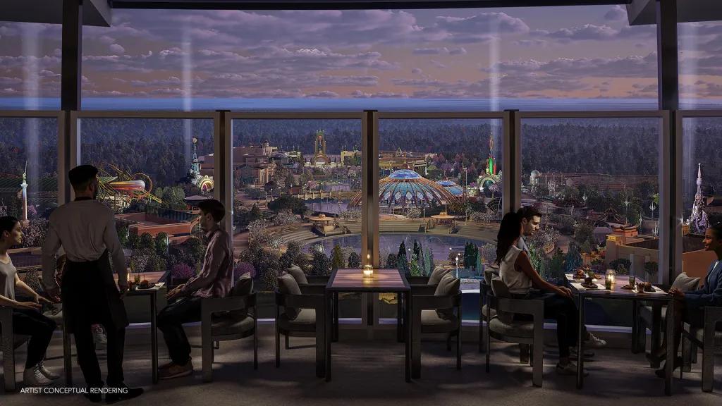 A circular rooftop bar offering 360 degree views of Epic Universe. There are people sat at candlelit tables by the edge of a glass window. There are also two white lights shooting up into the sky in the background.