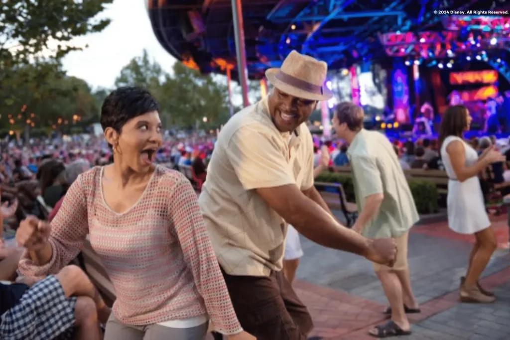Woman laughing dancing back to back with a man with other people dancing in the background. There is a stage as well.