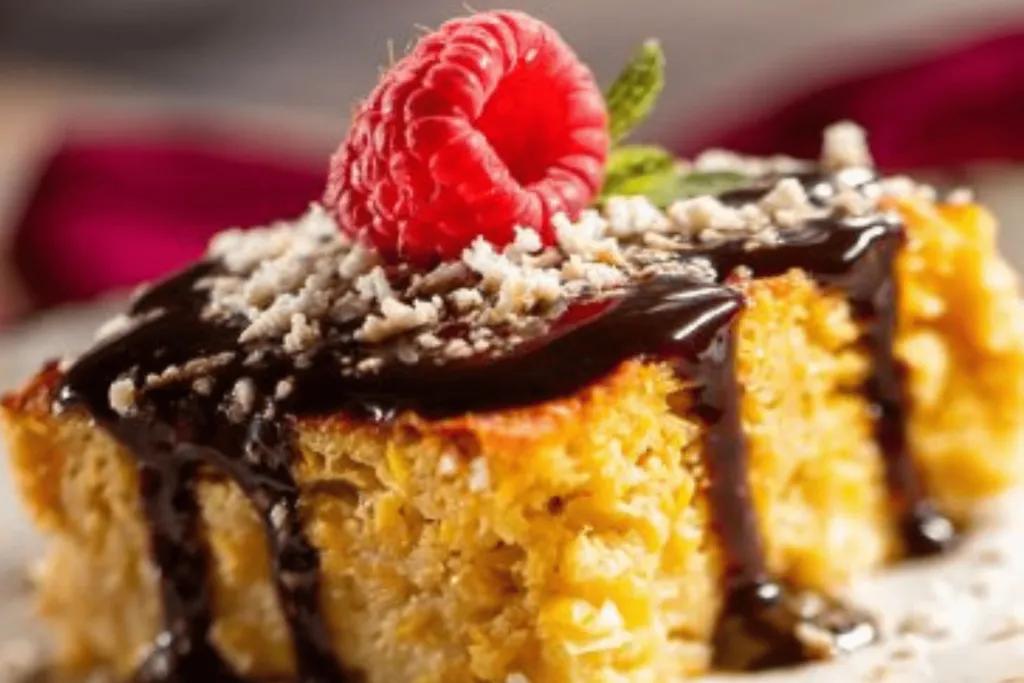 Yellow coloured cake with chocolate sauce dripping down and white powder on top. There is also a raspberry on top and some green leaves.
