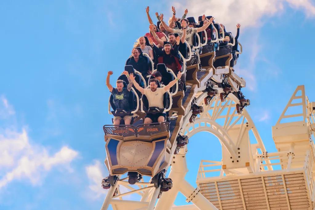A ride train full of people with their hands in the air going over a hill on a rollercoaster