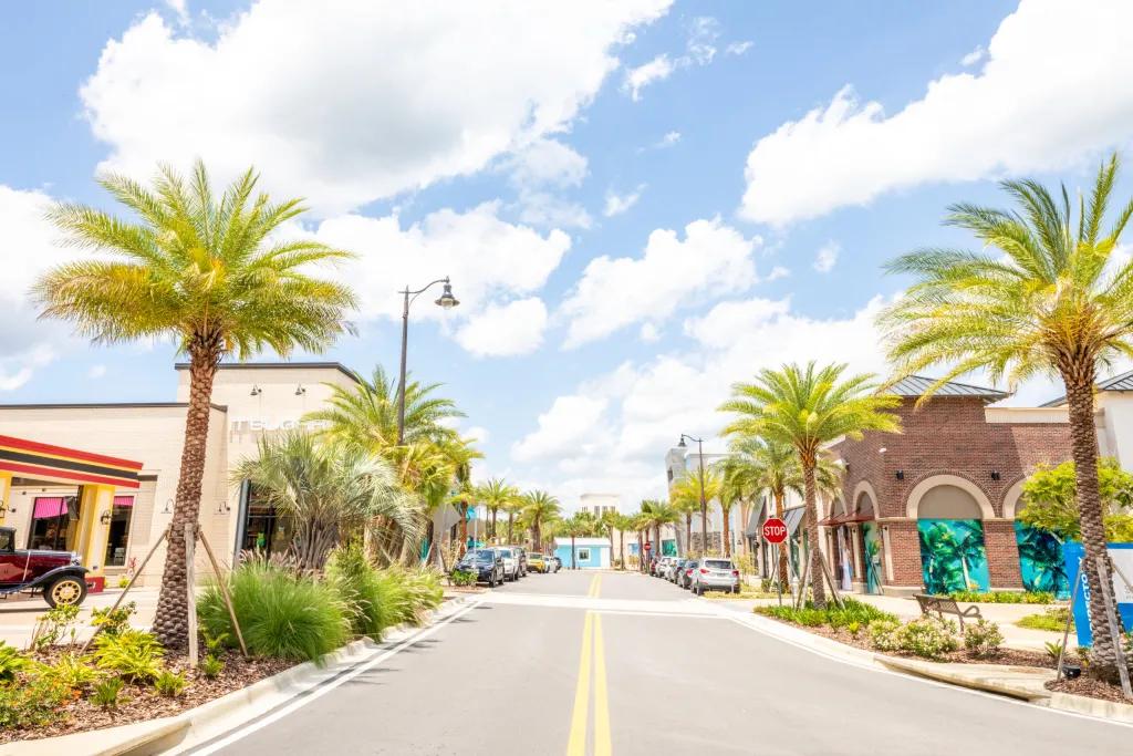 A road lined with palm trees in front of shops and restaurants