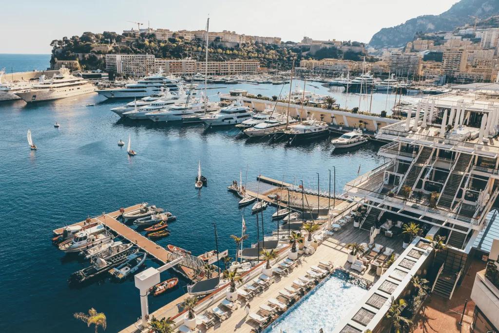 Many yachts docked up in the Monaco harbour. Behind there is a pretty mountain.