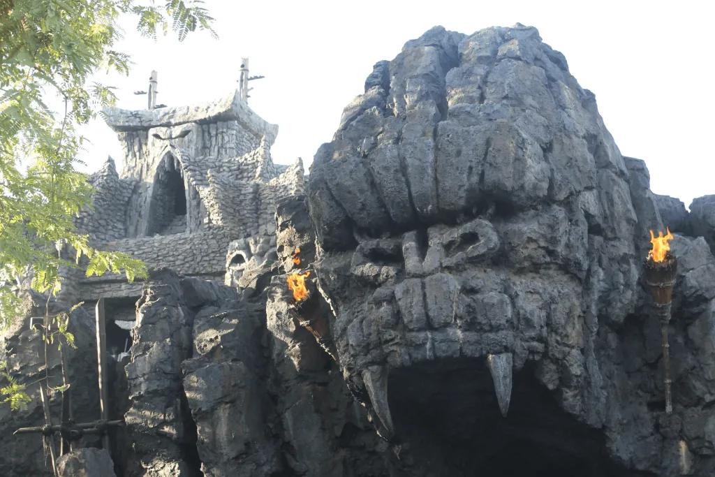 Giant grey rock shaped like gorilla face roaring. The mouth is a cave opening and either side of the entrance there are fire torches.