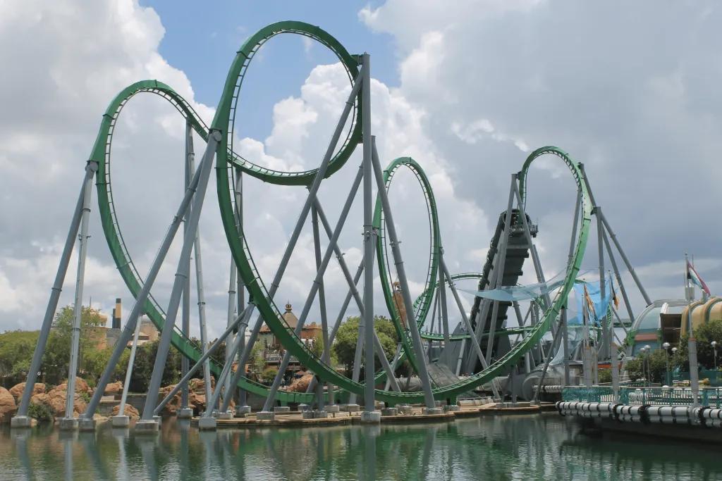 Green rollercoaster with large pretzel loop and a green tunnel which launches the coaster up in the air. There is a large lake beside this roller coaster.