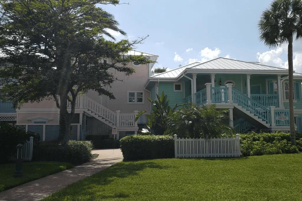 Two large coloured villas, one pastel pink and the other baby blue. The grass in front is pristine and they are decorated with white panels.