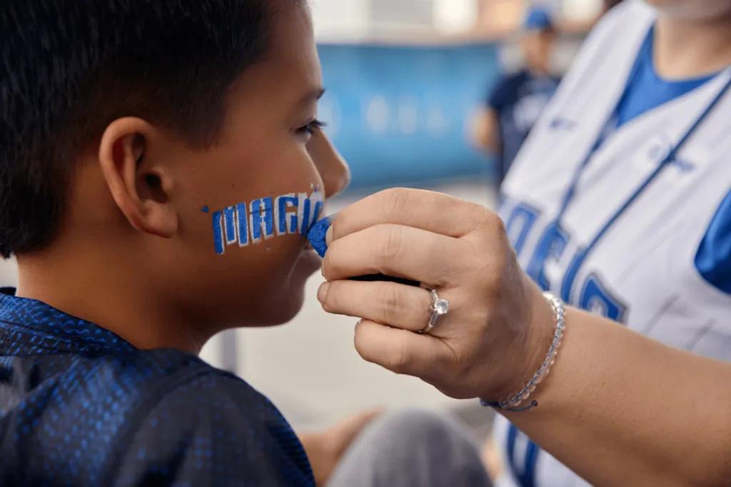 A young boy getting his face painted with the Orlando Magic logo