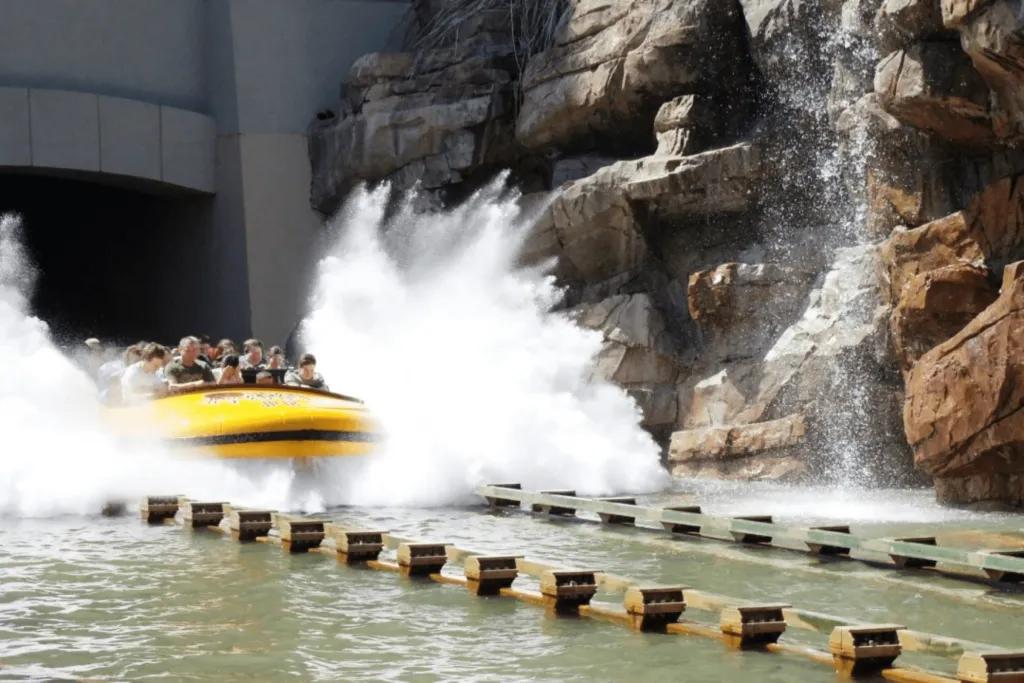 Big yellow boat splashing into a large body of water after plummeting down tall drop.