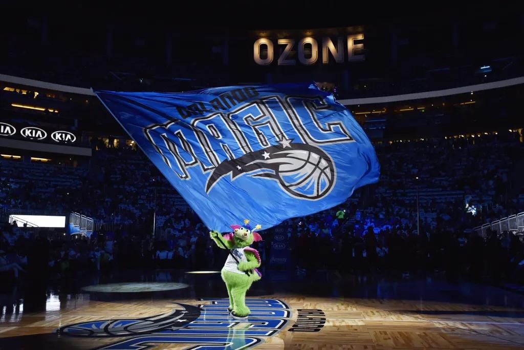Stuff the Dragon mascot holding the Orlando Magic flag on a basketball court