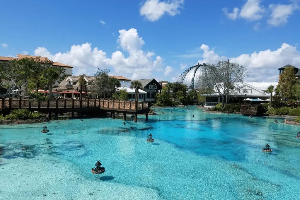 There is a crystal clear lake with fountain cannons. In the background there is a wooden pier and a spherical metal building.