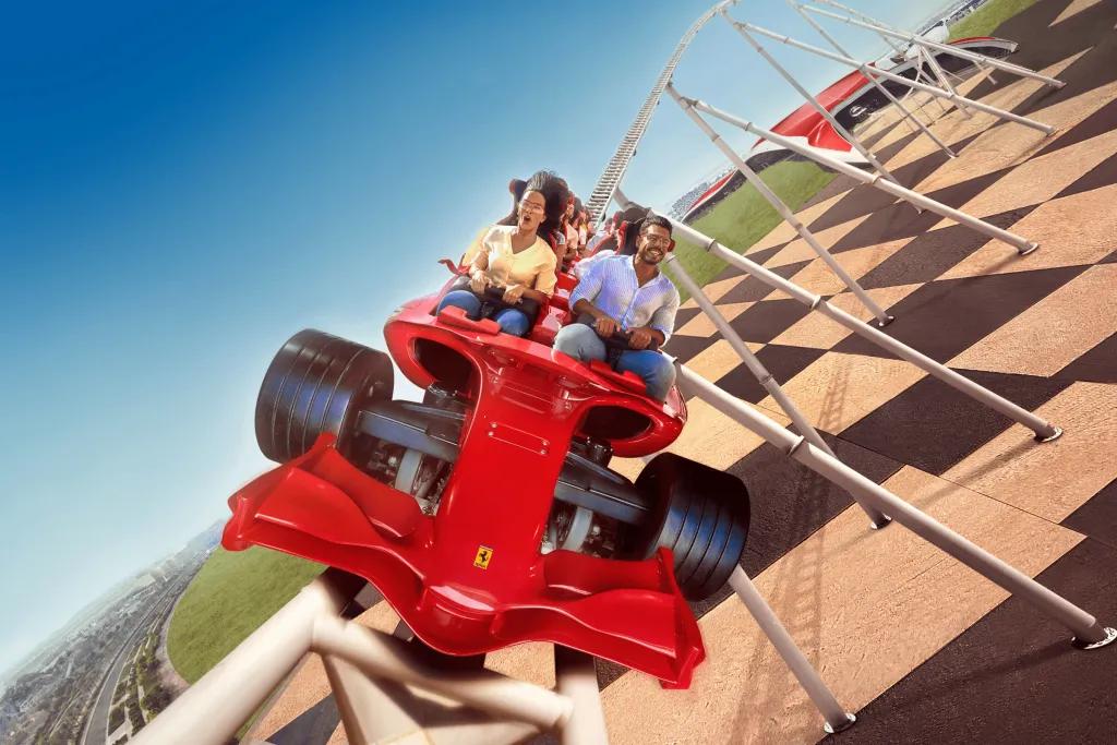 Two adults on a high speed rollercoaster outside of the Ferrari red building on a coaster car shaped like a red Formula 1 car.