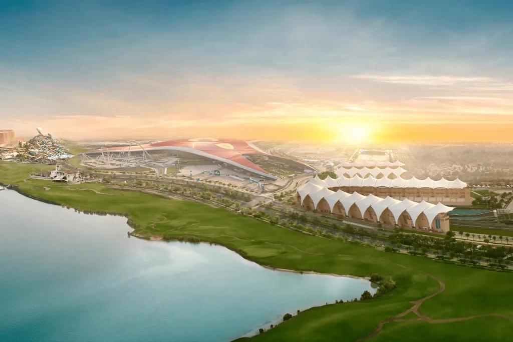 Sun setting over the Ferrari World complex. A large building with the yellow Ferrari logo and the f1 circuit. There is also a lake.