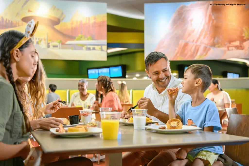 Family eating quick serve breakfast together in Disney's Art of Animation Resort. Little boy is eating bacon with his hands and the dad is smiling at him.
