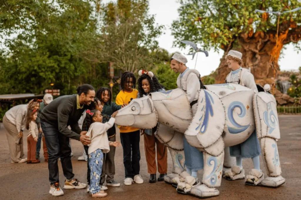 Two people dressed up in white costume with a huge polar bear puppet attached to them in front of the tree of life. There are kids petting the polar bear and the parents are crouched down smiling.