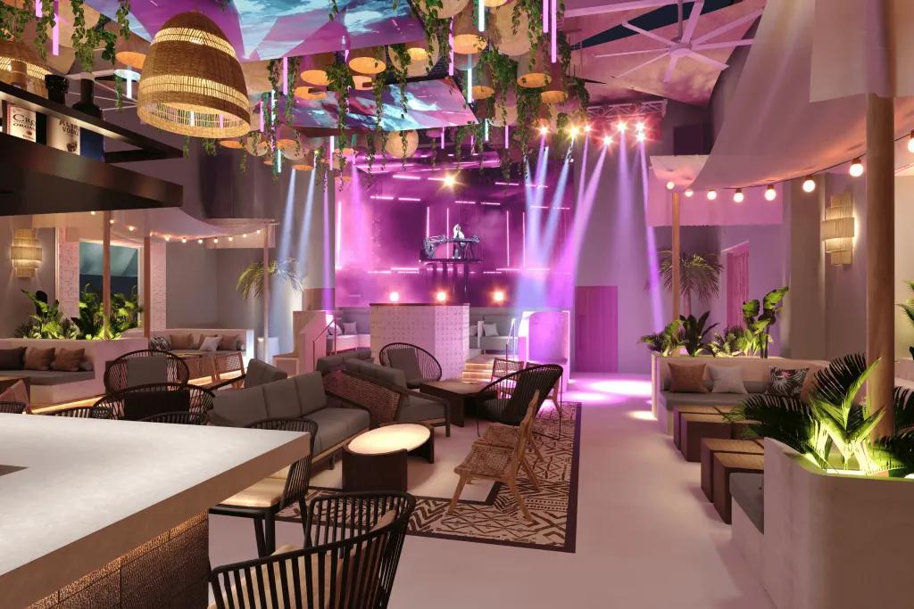 There is a modern bar with black stools and a white bar top. There are large beige lights and a quirky curved ceiling. There are pink performance spotlights coming down on top of a dj deck.