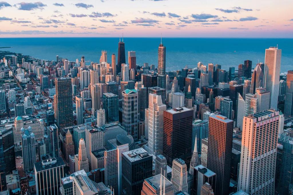 A large city full of tightly packed skyscrapers, coloured white and brown, glowing as the sunsets. In the background, you can see the sea as this is city is on the coast.