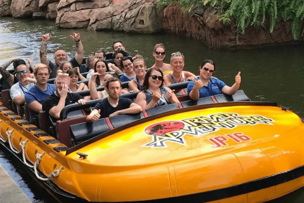 A large yellow river raft which says Jurassic Park River Adventure on the front. Riders look happy with their arms up in the photo.