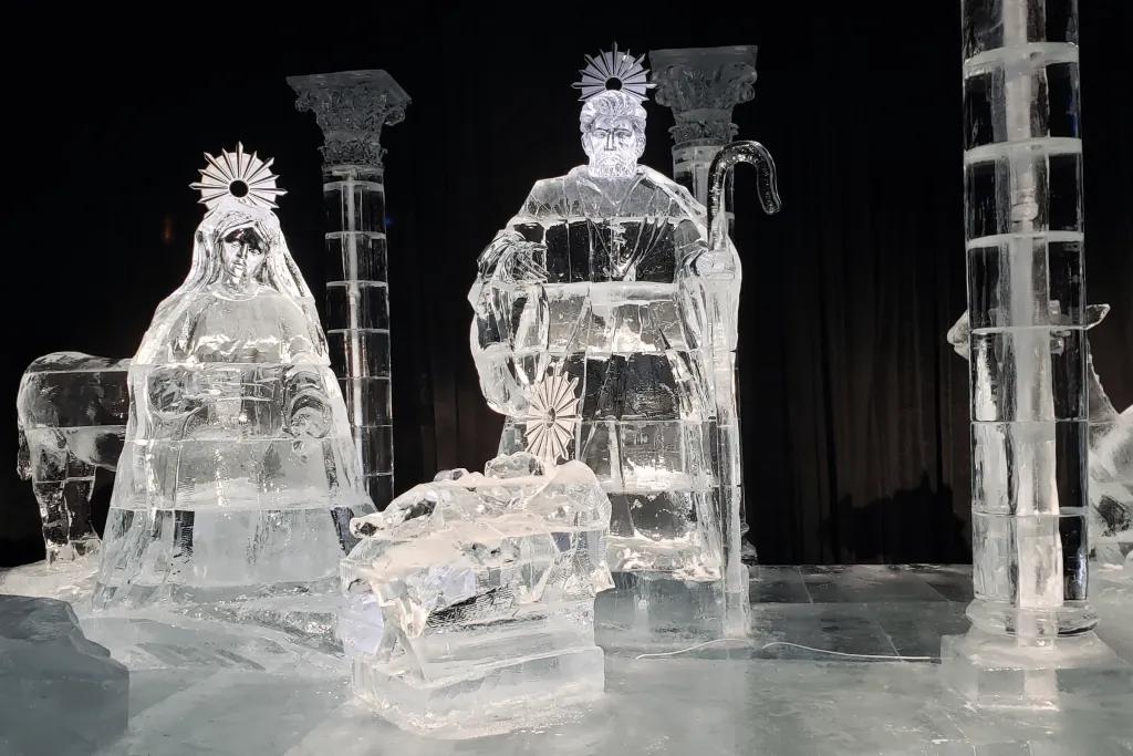 Ice sculpture of nativity scene, including Mary, Joseph and baby Jesus laying in a cot in a stable.