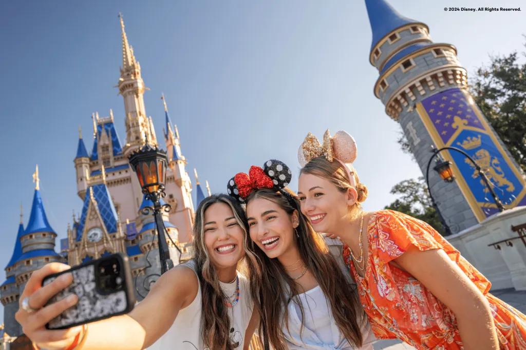 Three girls in front of Cinderella Castle in Magic Kingdom Park (big blue and pink pastel coloured castle). They are wearing different mickey ear headbands on their heads.