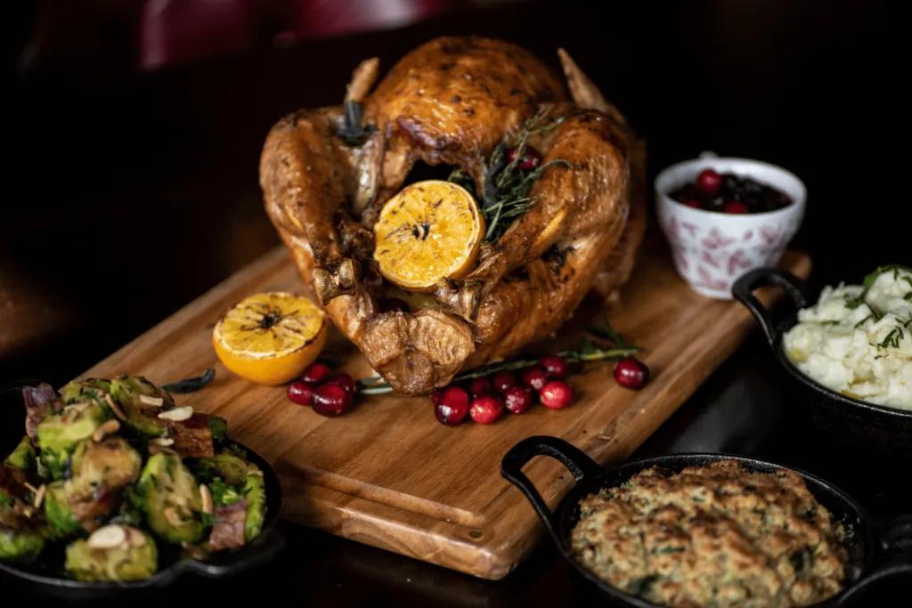 Roast chicken on a wooden board and there are sides such as mashed potato, vegetables and mac and cheese