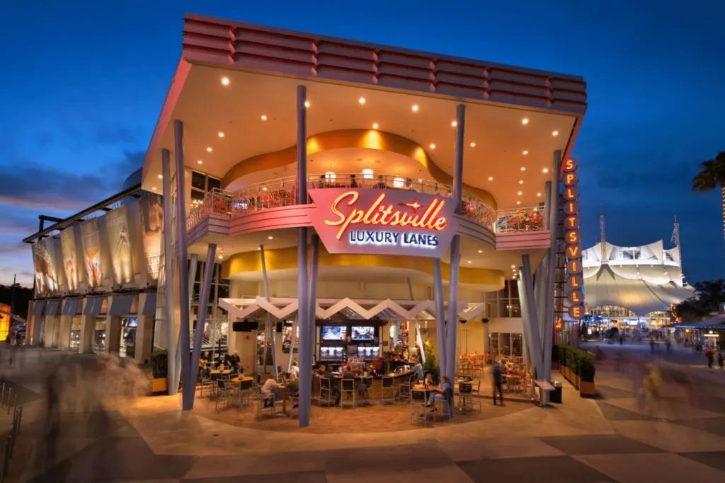 Large modern building with bar outside and people sat drinking. There is a giant neon red sign saying 'splitsville luxury lanes' on it.