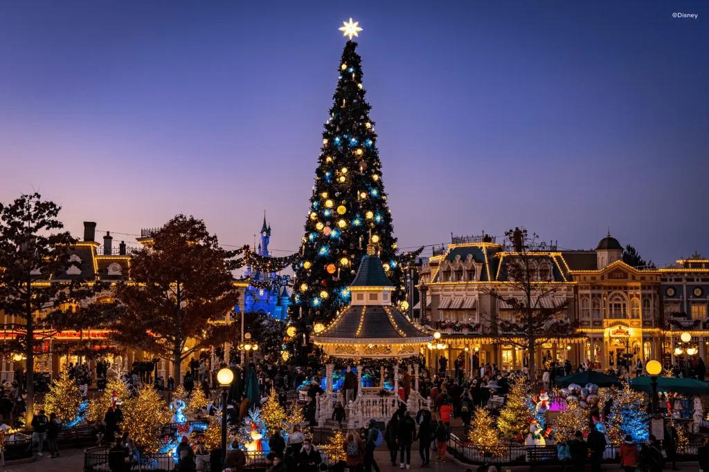 Sun setting over a theme park with a huge christmas tree in the centre of old fashioned buildings.
