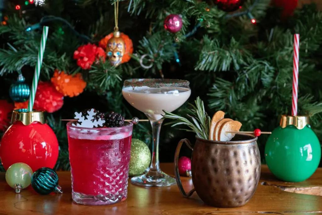 Behind there is a christmas tree with baubles of different colours. There are also 5 different cocktails in different glasses.
