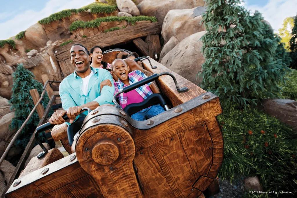 Guests sat in a mine cart coming out of a rock cave screaming and smiling.