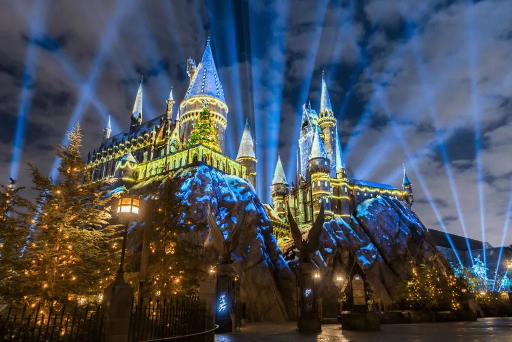 Hogwarts castle lit up in projections of golden christmas trees with loads of spotlights shooting up into the nightsky.