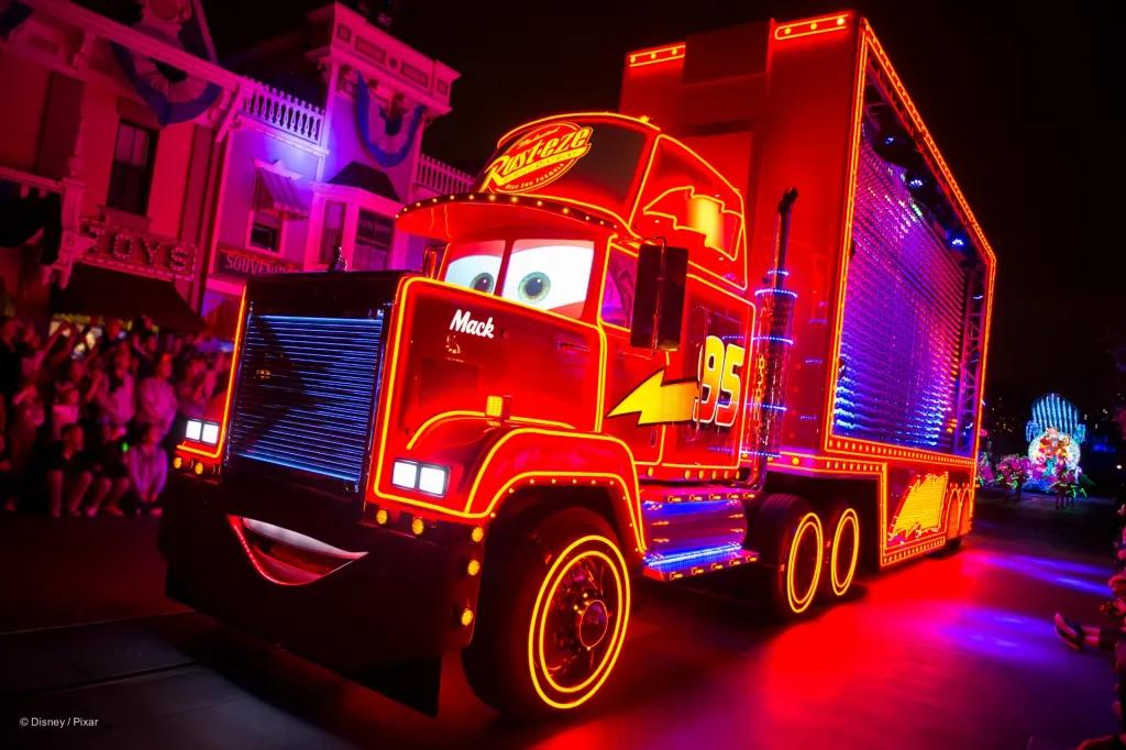 Mac from Cars, a giant red truck with a face on the front smiling illuminated with red neon  lights. He is decorated with yellow lightning bolts.