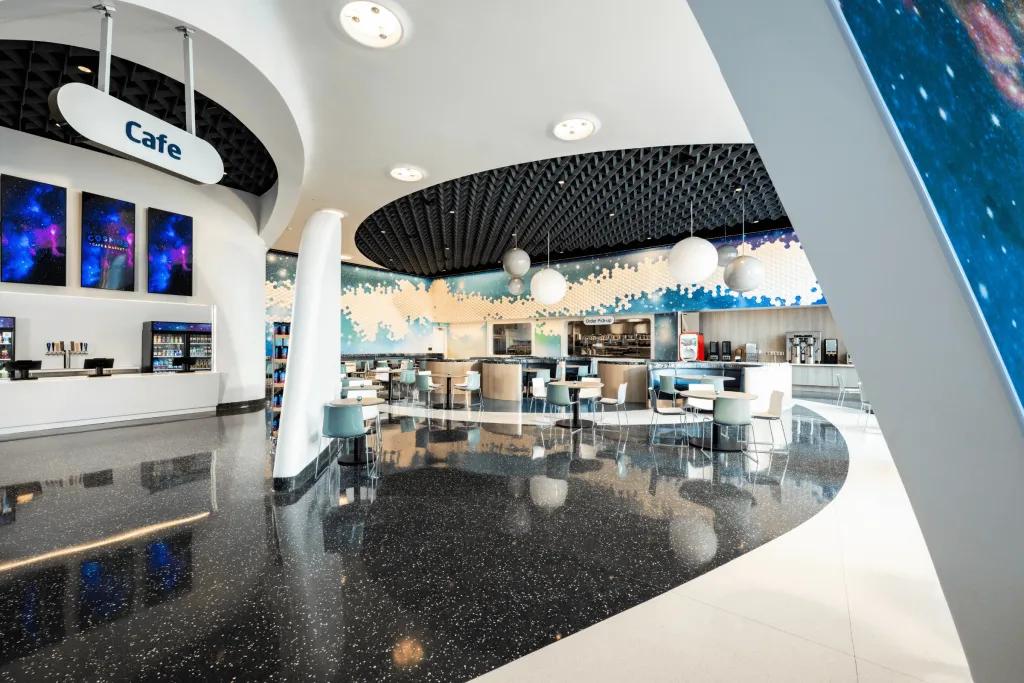 Open space cafe styled in a modern design and with star wall paper designs. There are tables for people to dine at and a sign where the food is served saying cafe!