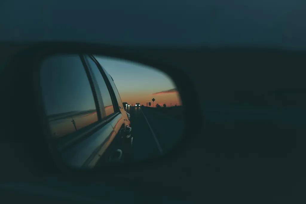 Dark night with car mirrors and in the mirror you can see the sun setting in the background and palm trees.
