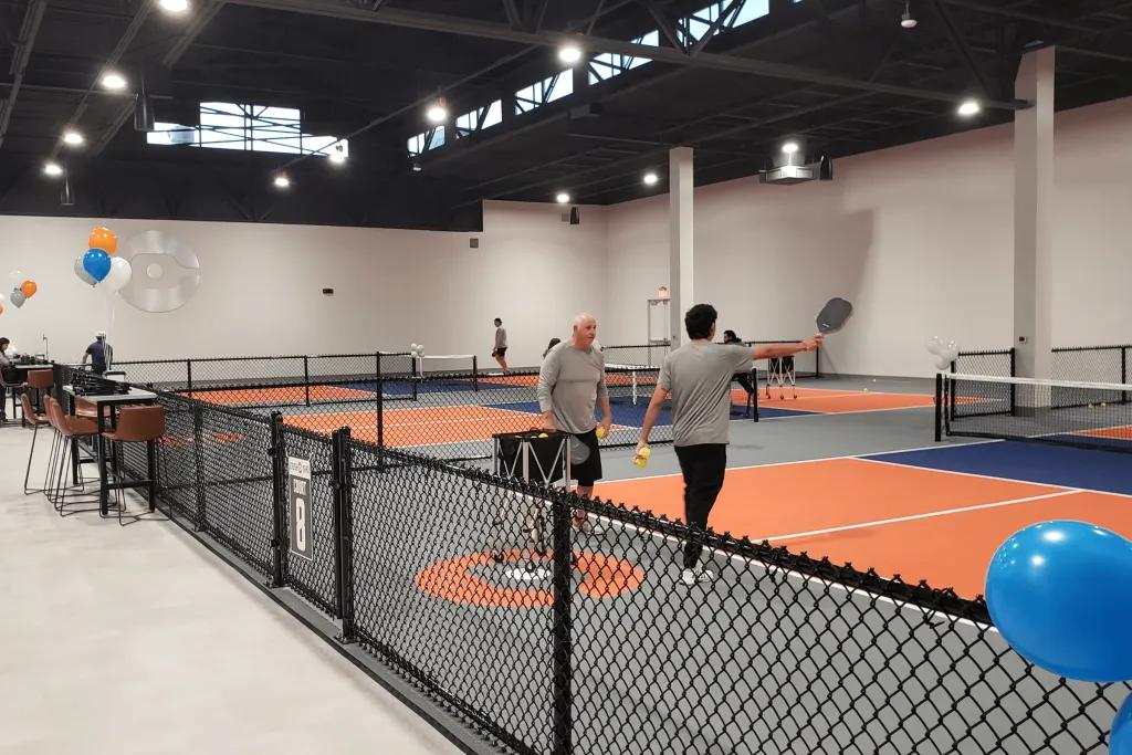 People stood with rackets drinking water in the middle of courts which are smaller than regular tennis courts. 