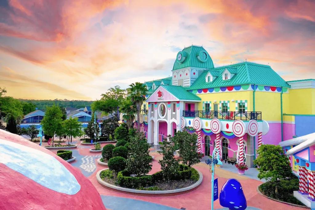 A large centre building coloured bright pink, yellow and turquoise shaped like a town hall. There are roads which are wheelchair accessible and a large mushroom with a carousel under it.