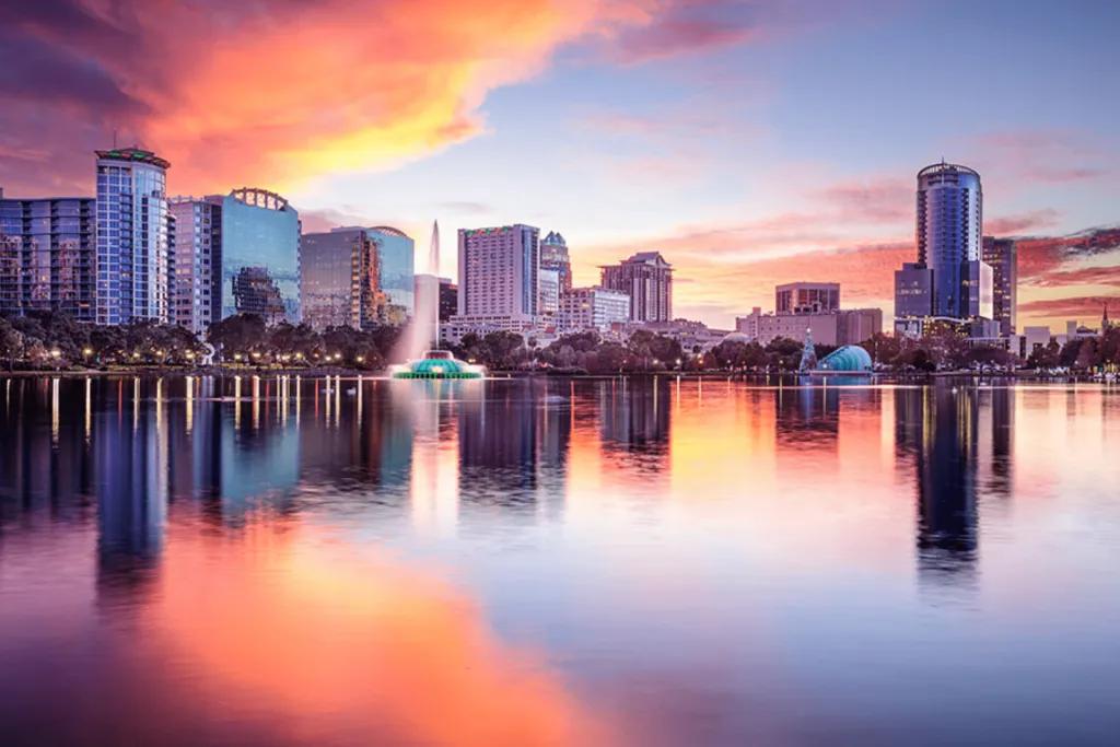 Huge lake at sunset with the orange sun reflections lighting up the sky above large glass buildings.