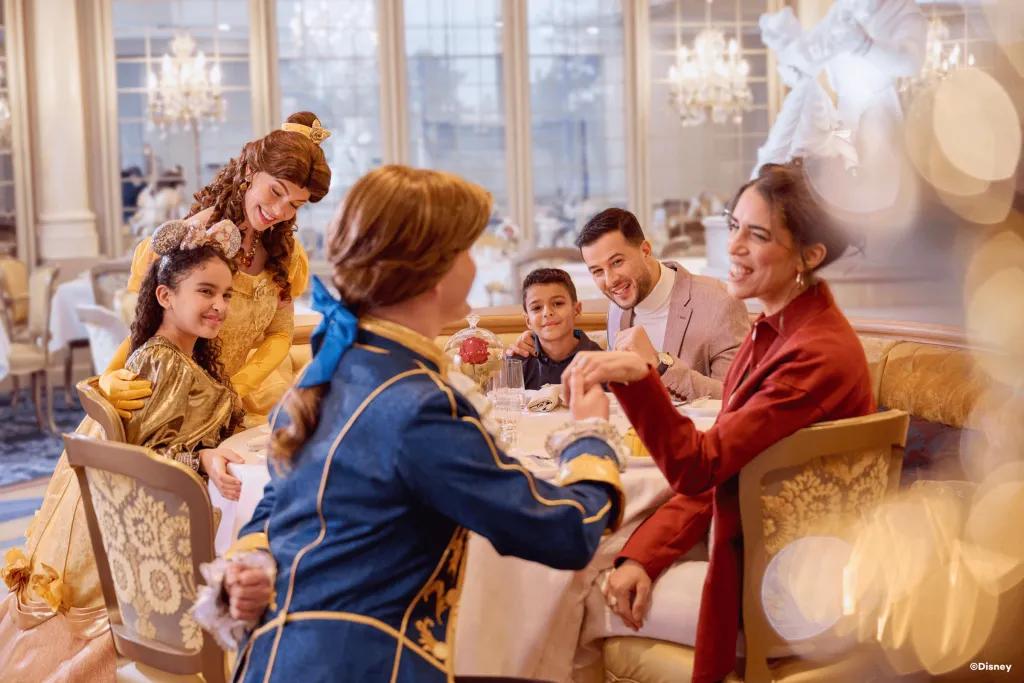 A family sat around a table in a restaurant being greeted by Belle and her prince