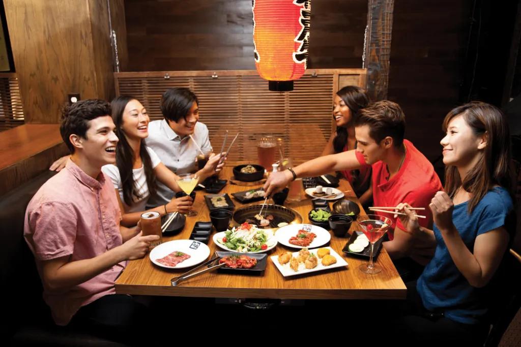 Group of friends sat around a table sharing dishes and drinking alcoholic drinks in Japanese style restaurants.
