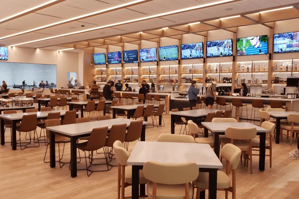 Cream coloured restaurant with bars lining the wall and multiple flat screen tvs.
