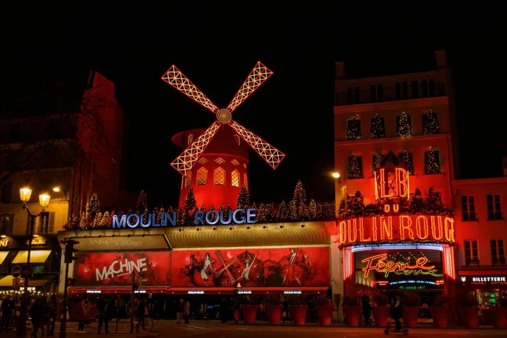 A large building lit red with a large windmill prop on top and a white sign saying Moulin Rouge