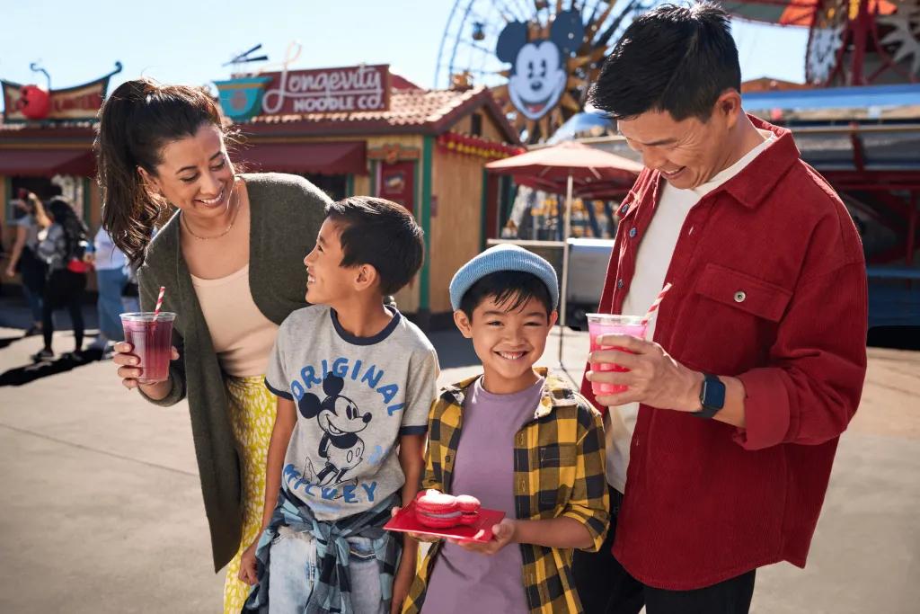 A family of four, with two sons holding food and drinks in front of Pixar Pier.