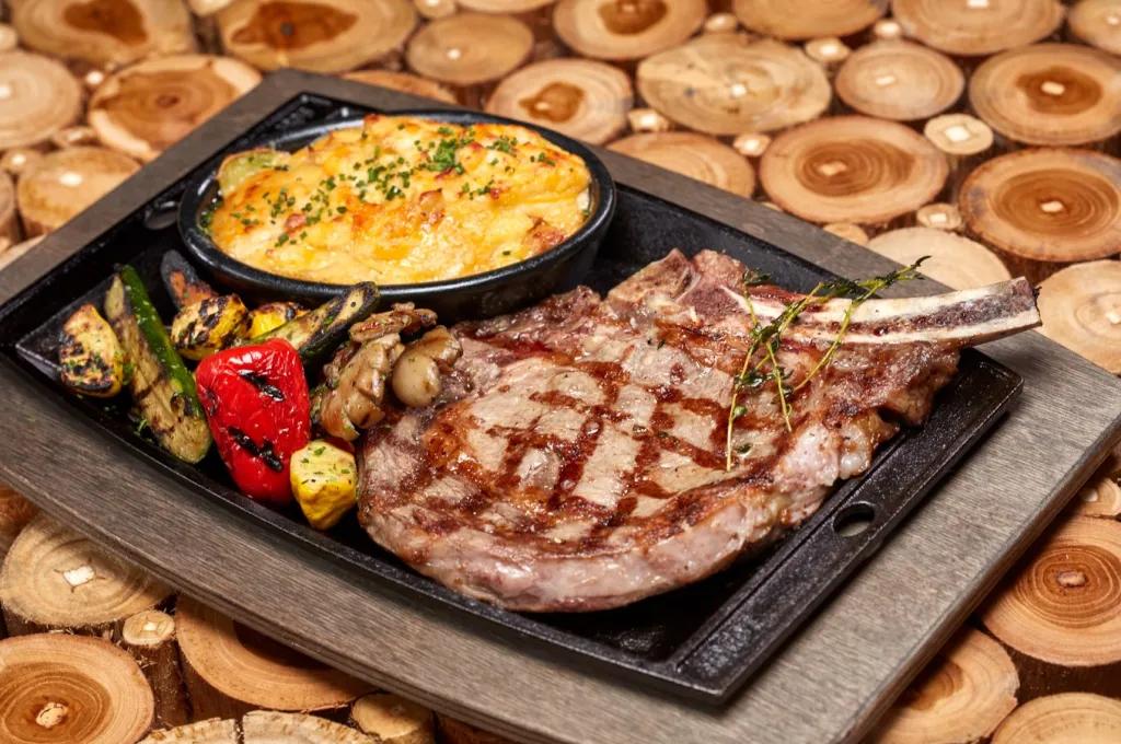 A ribeye steak, baked potato gratin and roasted vegetables on a cast-iron plate