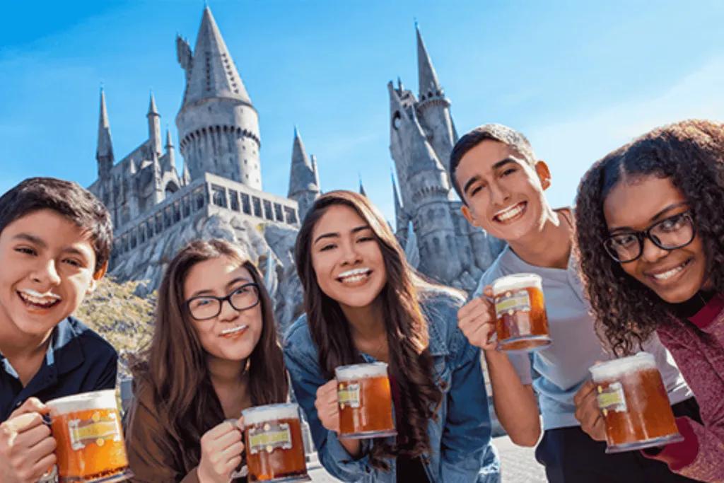 A group of young adults posing with mug of Butterbeer in front of Hogwarts castle