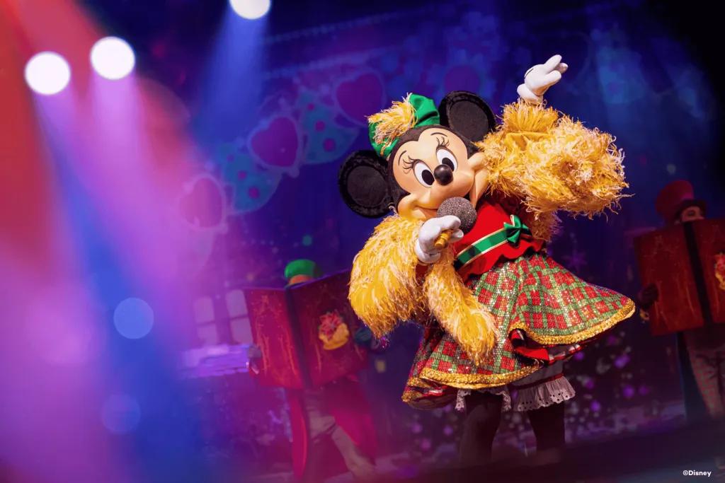 Minnie Mouse wearing a Christmas outfit and singing into a mic onstage